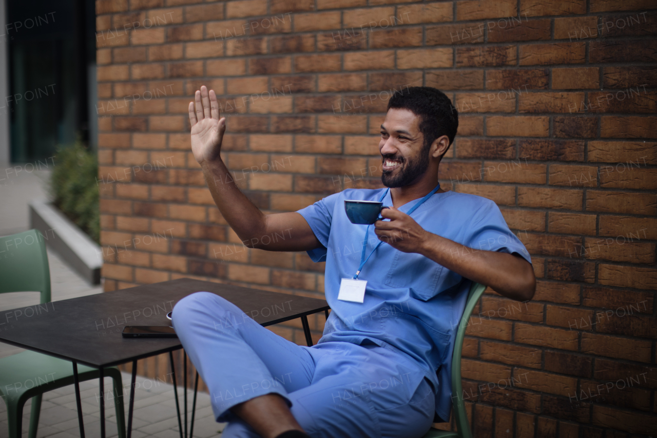 Nurse man sitting and waving for someone, outdoor at cafe.