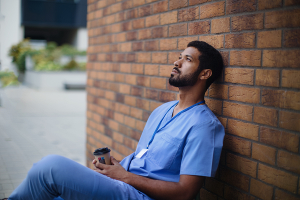 Tired caregiver man resting outdoor, in front of a nurishing home.