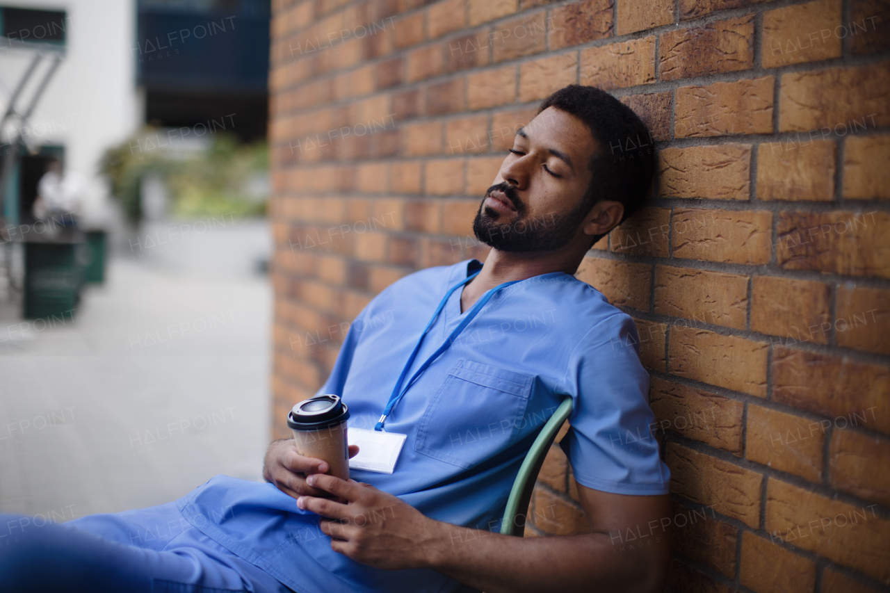 Tired caregiver man resting outdoor, in front of a nurishing home.