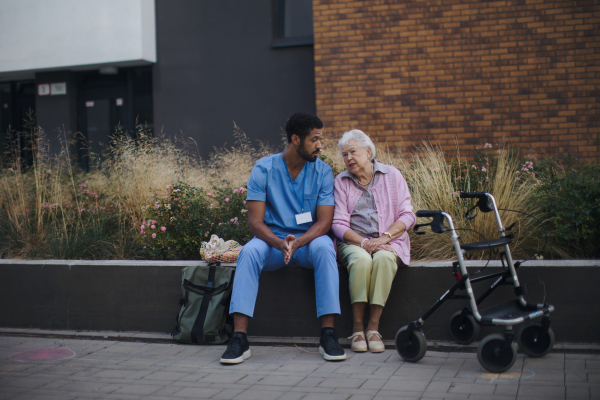 Happy senior woman sitting and talking with a medical assistant in front of nurishing home.