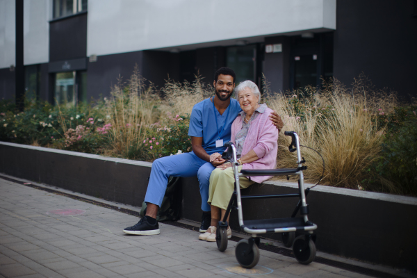 Happy senior woman sitting and talking with a medical assistant in front of nurishing home.