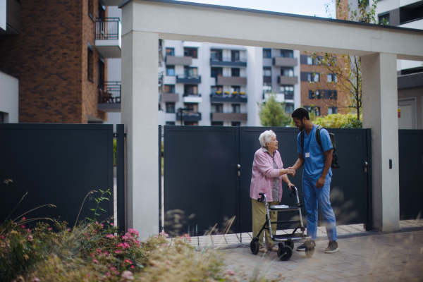 Caregiver walking with senior woman client in front of a nurishing home.