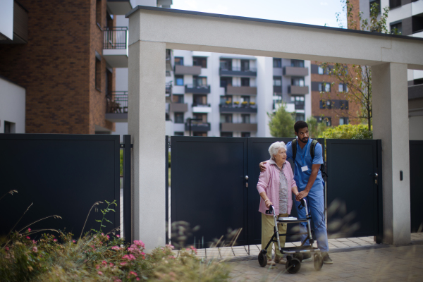 Caregiver walking with senior woman client in front of a nurishing home.