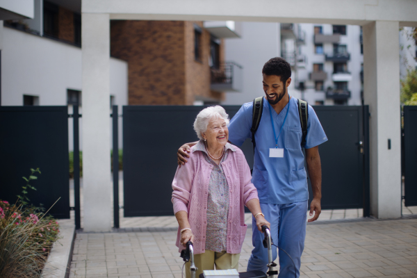 Caregiver walking with senior woman client in front of a nurishing home.