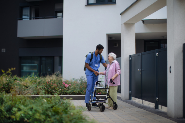 Caregiver walking with senior woman client in front of a nurishing home.