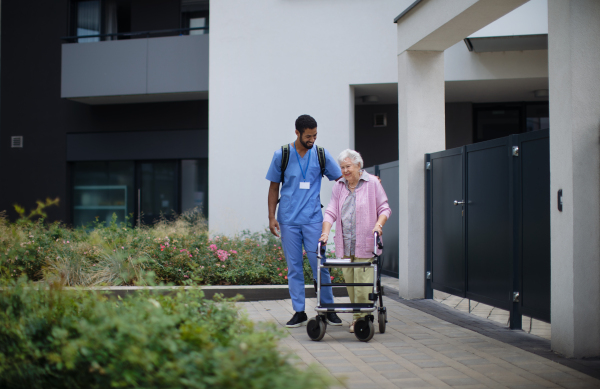 Caregiver walking with senior woman client in front of a nurishing home.