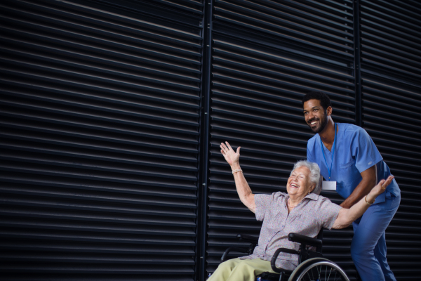 Caregiver man pushing excited senior woman at wheelchair on a street, enjoying time together.