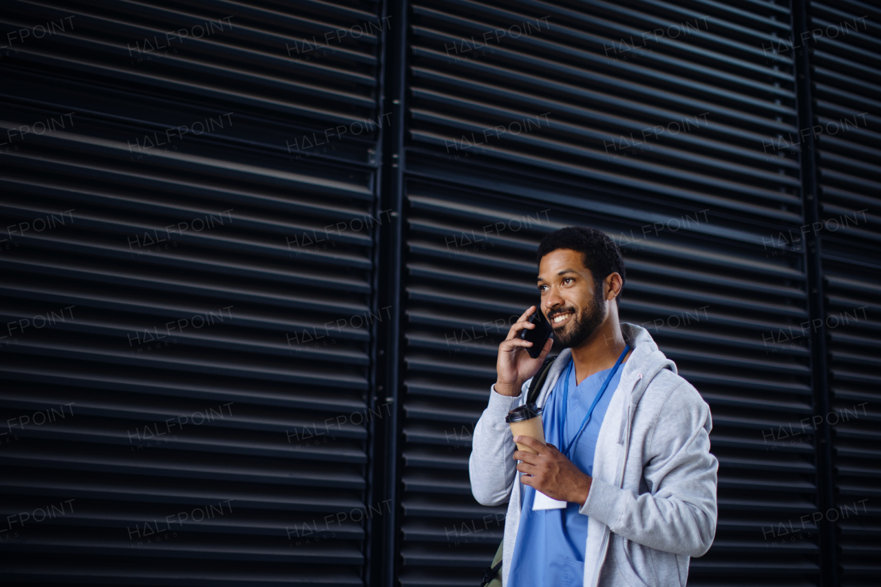 Young multiracial man working as nurse coming back from work, calling and holding a cup of coffee.