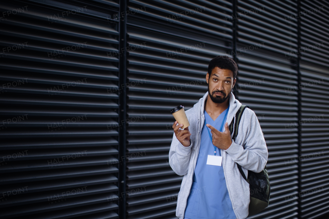 Young multiracial man working as nurse coming back from work and holding cup of a coffee.