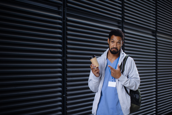 Young multiracial man working as nurse coming back from work and holding cup of a coffee.