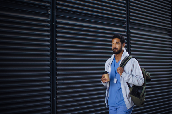 Young multiracial man working as nurse coming back from work and holding cup of a coffee.