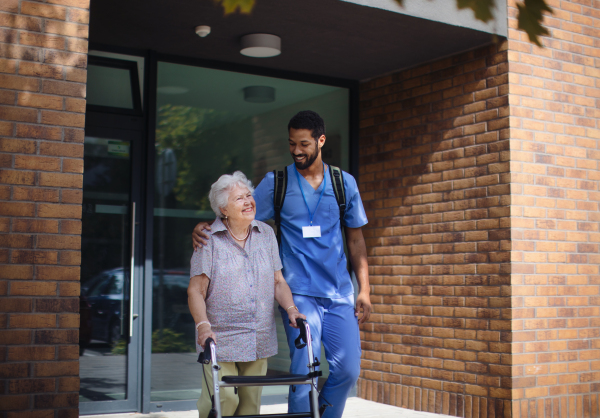 Caregiver walking with senior woman client in front of a nurishing home.