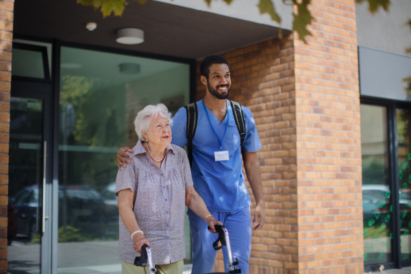 Caregiver walking with senior woman client in front of a nurishing home.