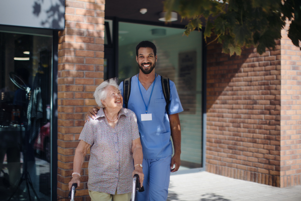 Caregiver walking with senior woman client in front of a nurishing home.