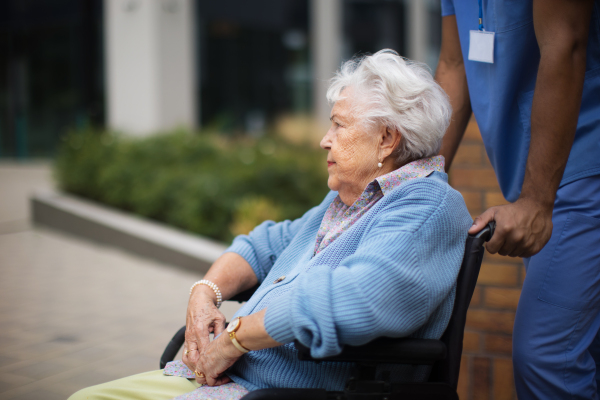 Portrait of senior woman at a wheelchair spending time outside with her assistant.