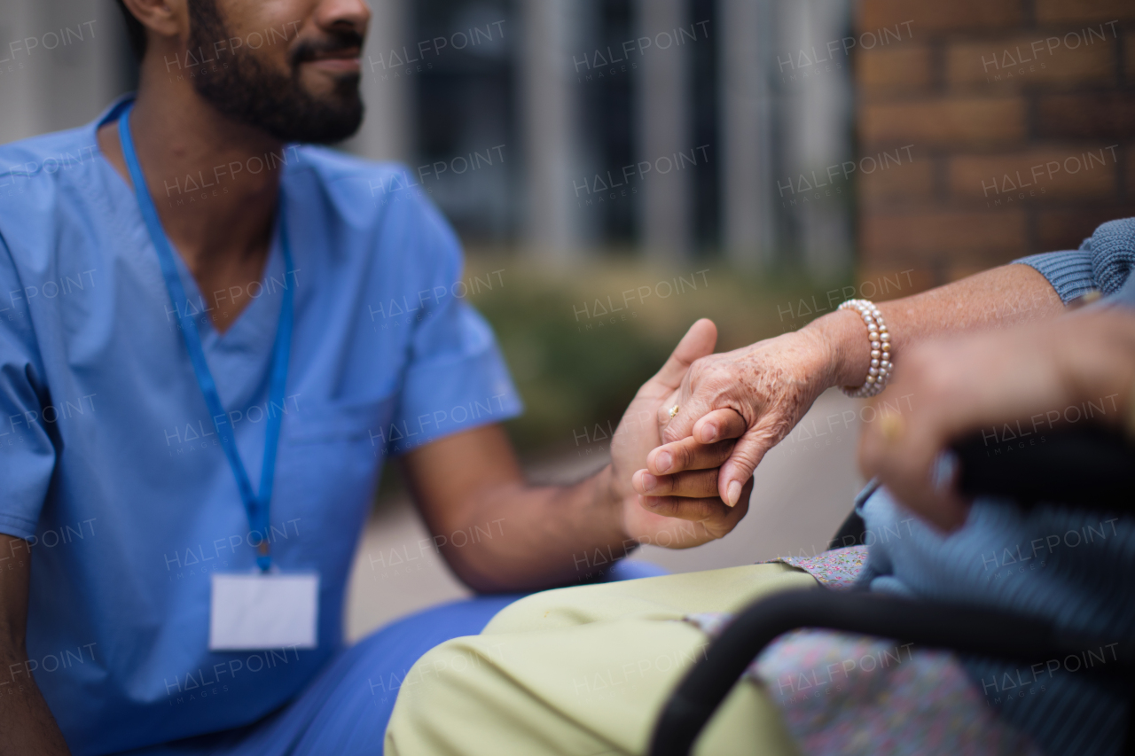 Close-up of caregiver holding hand of his client on a wheelchair.