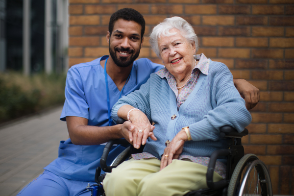 Happy senior woman at a wheelchair spending time outside with her assistant.