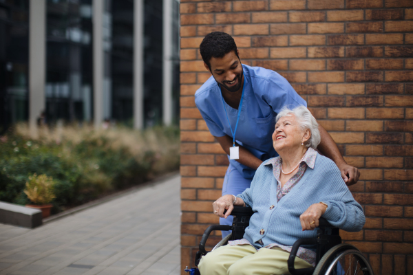 Happy senior woman at a wheelchair spending time outside with her assistant.