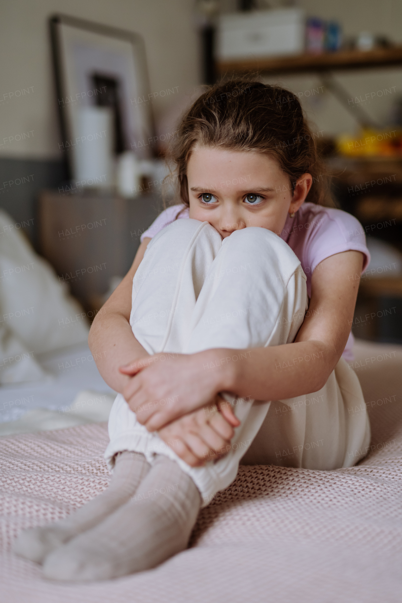 Little sad girl sitting alone on bed.