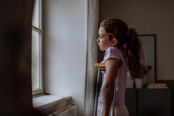 Little girl with broken leg looking trough the window.