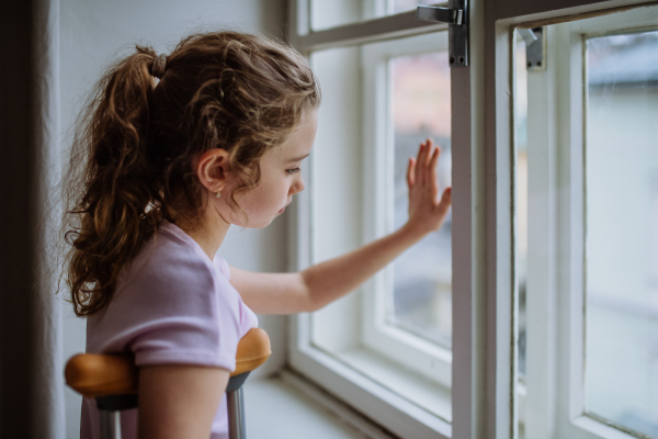 Little girl with broken leg looking trough the window.