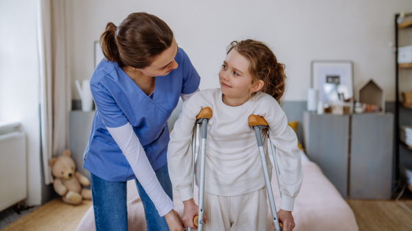 Young nurse helping to walk to little girl with a broken leg.