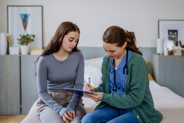 Teenage girl having stomach ache, young woman doctor examining her.