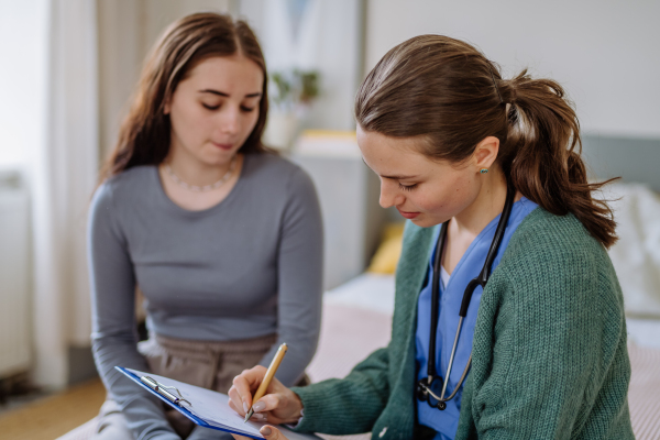 Teenage girl having stomach ache, young woman doctor examining her.