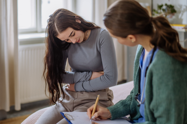 Teenage girl having stomach ache, young woman doctor examining her.