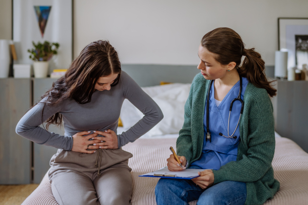 Teenage girl having stomach ache, young woman doctor examining her.