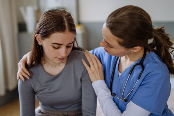 Young nurse taking care of a teenage girl, consoling her.