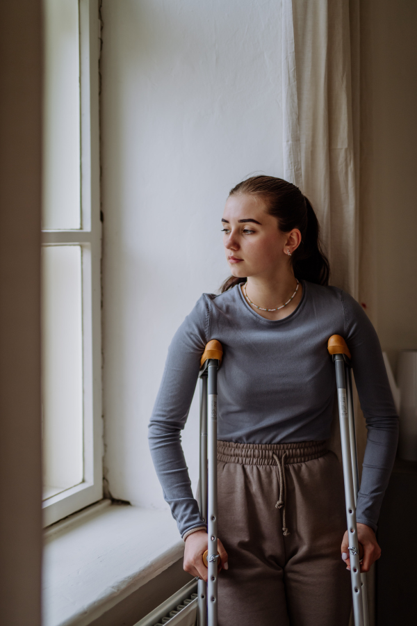 Teenage girl with broken leg looking trough the window.