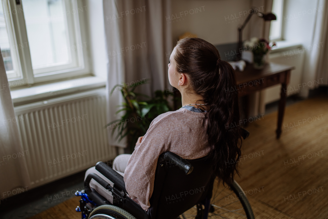 Unhappy teenage girl sitting on wheelchair and looking out of the window.