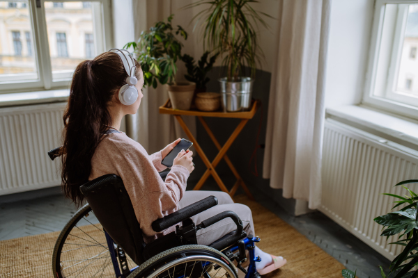 Unhappy teenage girl sitting on wheelchair and looking out of the window.