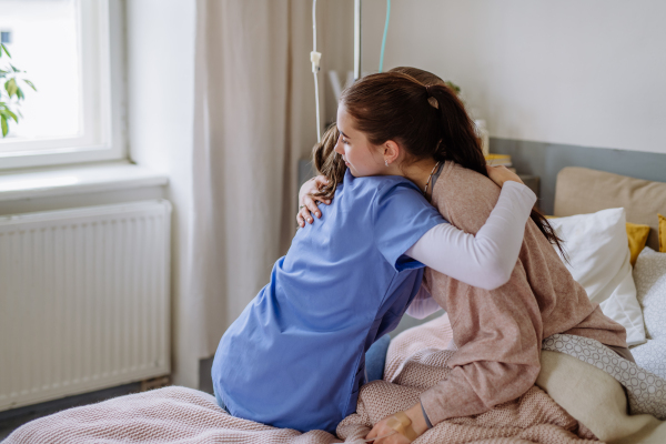 Young doctor consoling teenage girl in a hospital room.