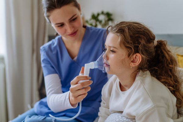 Little girl with inhaler in hospital room, a nurse chcecking her.