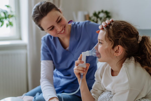 Little girl with inhaler in hospital room, a nurse chcecking her.