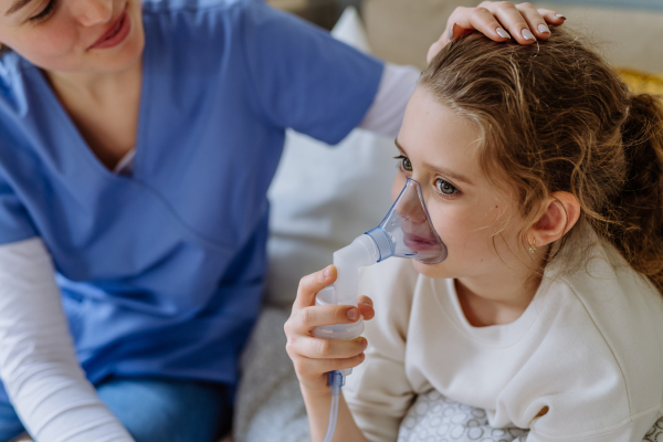 Little girl with inhaler in hospital room, a nurse chcecking her.