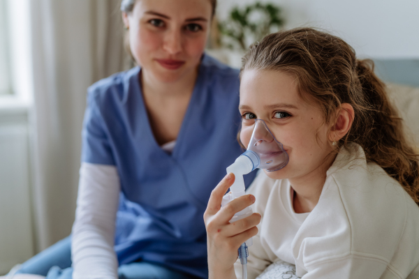 Little girl with inhaler in hospital room, a nurse chcecking her.