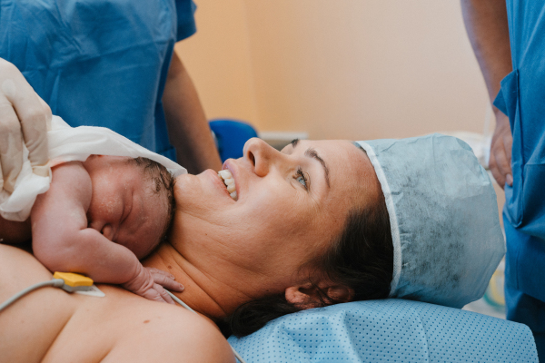 Happy mother bonding with newborn baby right after birth by c-section. Bonding on operating room. Skin to skin contact.