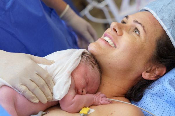 Happy mother bonding with newborn baby right after birth by c-section. Bonding on operating room. Skin to skin contact.