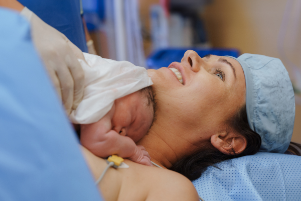 Happy mother bonding with newborn baby right after birth by c-section. Bonding on operating room. Skin to skin contact.