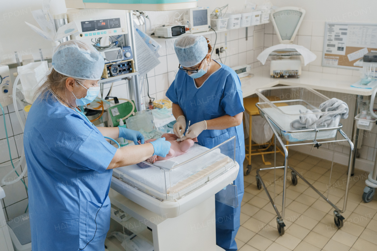 Neonatal nursers, doctor examining newborn baby, taking care of infant after birth. Cutting umbilical cord. Neonatal care, newborn's health and well-being.