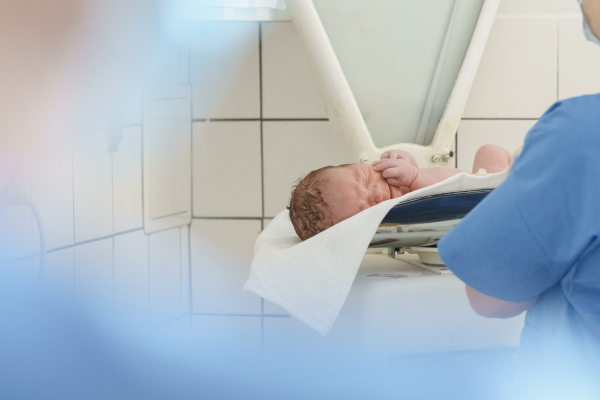 Neonatal nursers, doctor weighing and examining newborn baby, taking care of infant after birth. Neonatal care, newborn's health and well-being.