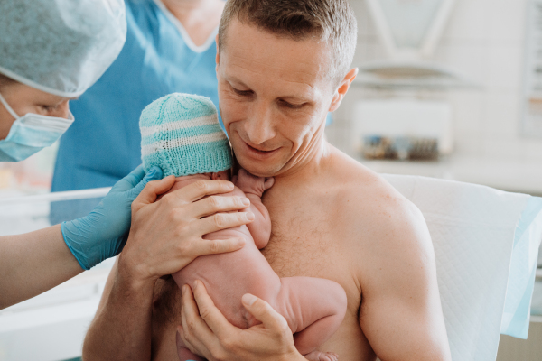 Nurse helping father to hold newborn baby right after birth. Skin to skin, bonding for proud dad.