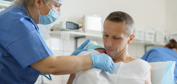 Nurse helping father to hold newborn baby right after birth. Skin to skin, bonding for dad. Banner with copy space.