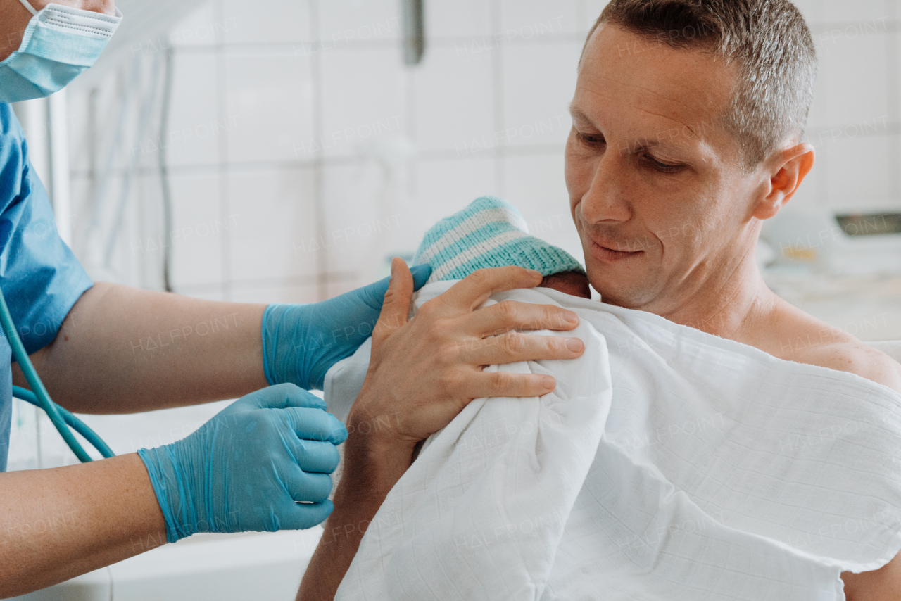 Nurse helping father to hold newborn baby right after birth. Skin to skin, bonding for proud dad.