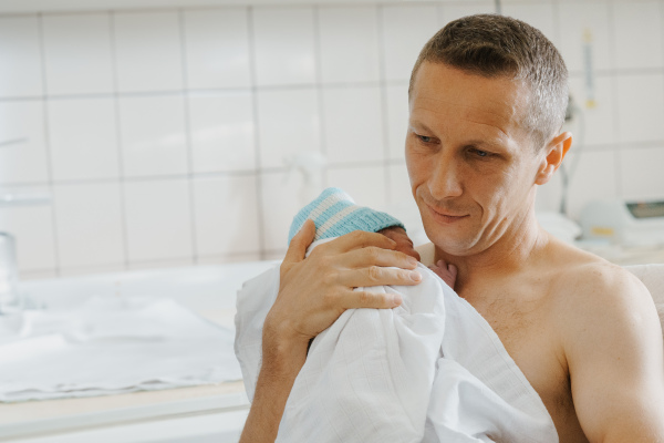 Proud father bonding with newborn baby right after birth. Holding baby for the first time. Skin to skin contact.