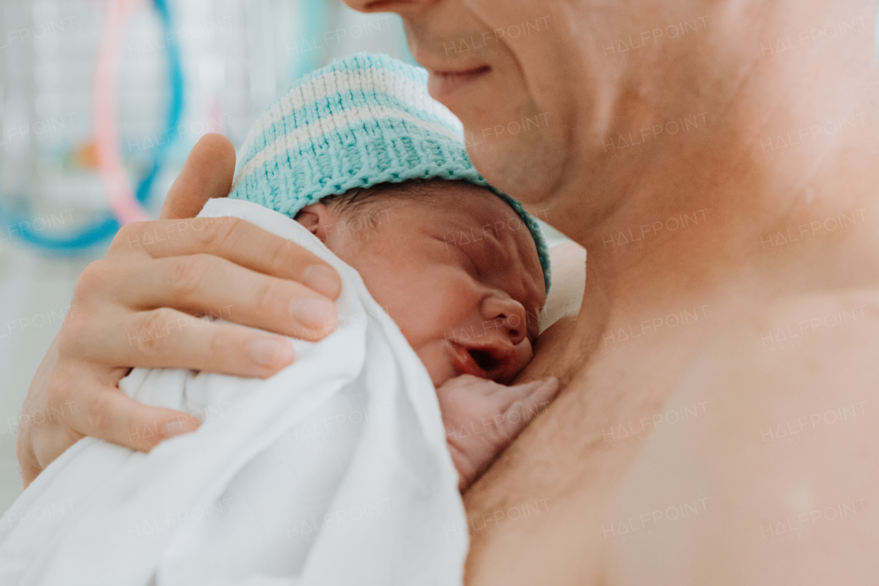 Proud father bonding with newborn baby right after birth. Holding baby for the first time. Skin to skin contact.