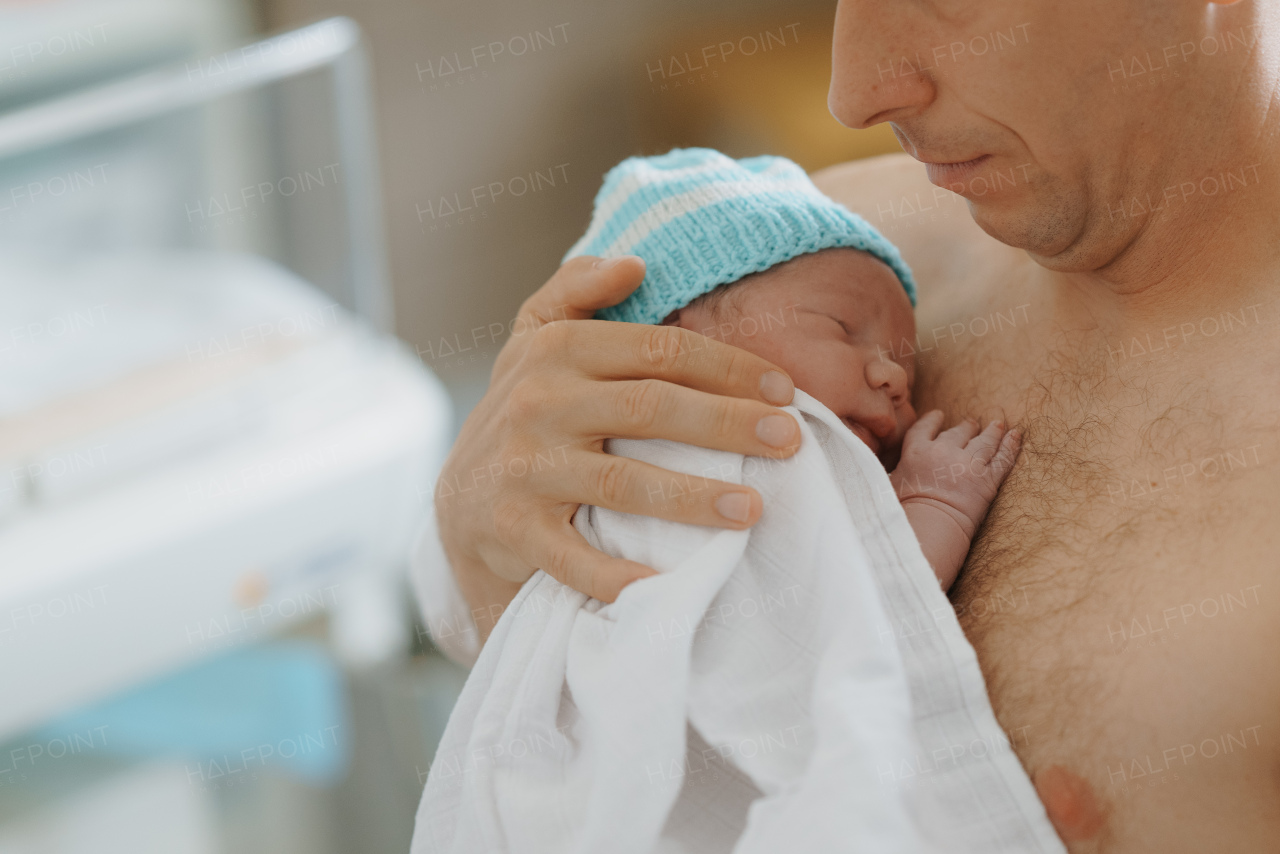 Proud father bonding with newborn baby right after birth. Holding baby for the first time. Skin to skin contact.